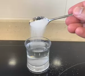 Hand pouring salt into a glass of water