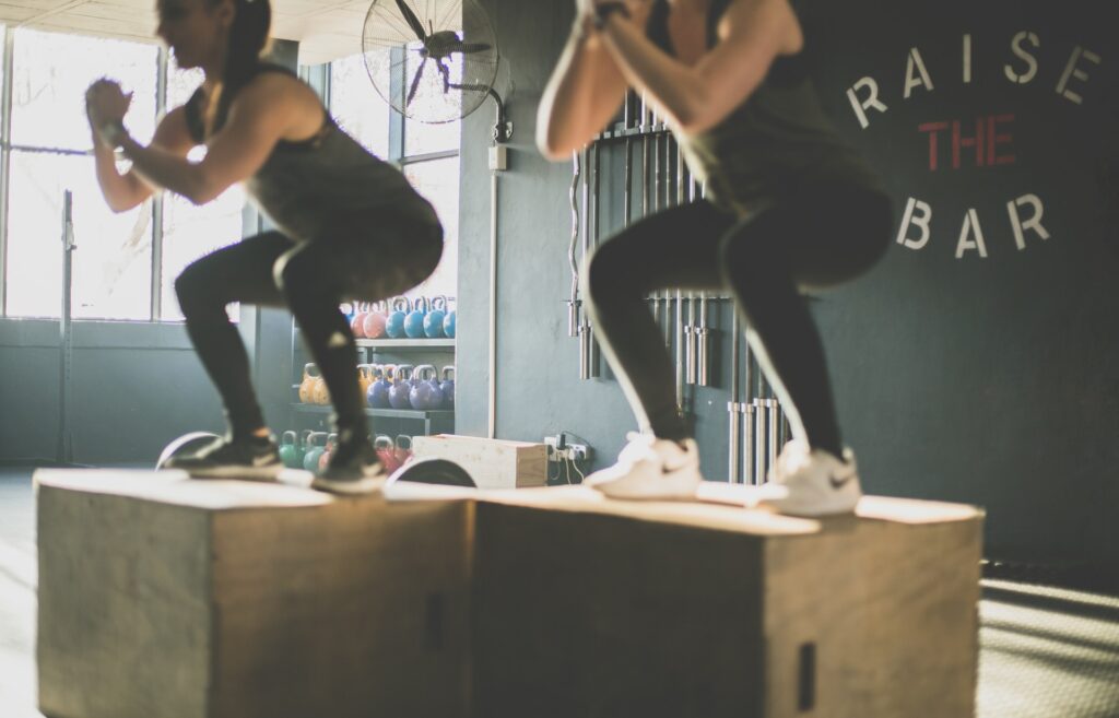 2 women doing bodyweight squats on CrossFit boxes